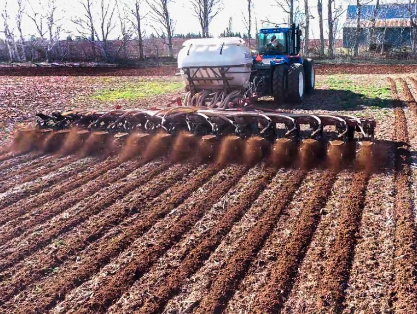 A tractor tills the soil, kicking up dirt in a field.